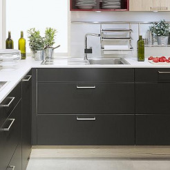 Schwarze L-Küche mit silbernen Griffen, weißer Arbeitsplatte und Holzregalen