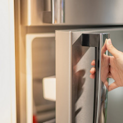 Hand am Griff eines Kühlschranks mit gebürsteter Edelstahloberfläche ohne Fingerabdrücke