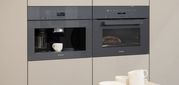 Miele Kompakt-Kaffeevollautomat und Backofen in Graphitgrau nebeneinander eingebaut in beiger Leicht-Küche