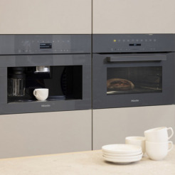 Miele Kompakt-Kaffeevollautomat und Backofen in Graphitgrau nebeneinander eingebaut in beiger Leicht-Küche