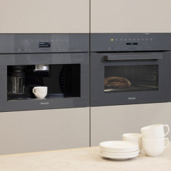 Miele Kompakt-Kaffeevollautomat und Backofen in Graphitgrau nebeneinander eingebaut in beiger Leicht-Küche