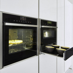 weisse grifflose Küchenfront mit nebeneinander eingebautem Backofen und Dampfgarer, darunter Wärmeschublade. Geräte von NEFF