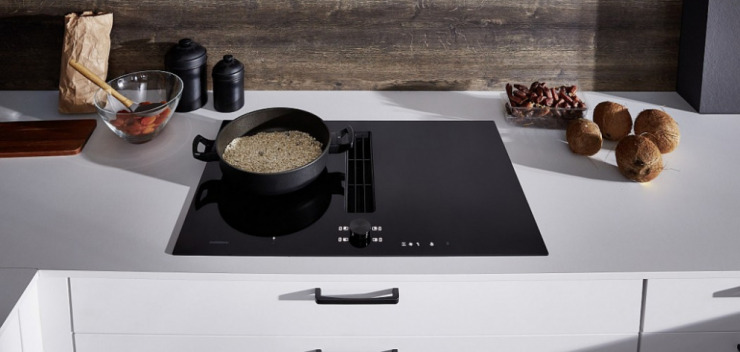 Gaggenau Induktionskochfeld in weißer Nobilia Küche darauf gusseiserner Topf mit Getreide darin umliegend Kokosnüsse und Datteln und getrocknete Aprikosen in einer Glasschale