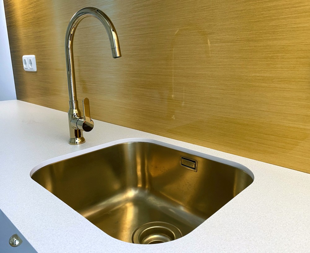goldfarbene Unterbauspüle mit goldenem Wasserhahn eingebaut in eine weiße Compact-Arbeitsplatte mit Quarzkeramik-Dekor in einer Mini-Küche in Berlin
